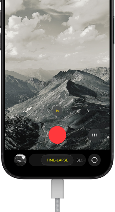 iPhone 18 Pro, Vorderseite, das Display zeigt eine Berglandschaft, mit der Kamera Modus Überlagerung im Zeitraffer Modus, mit dem Netzkabel am Ladeanschluss