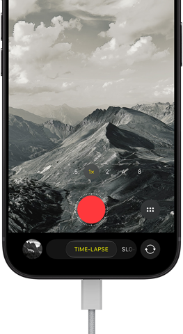 iPhone 18 Pro, Vorderseite, das Display zeigt eine Berglandschaft, mit der Kamera Modus Überlagerung im Zeitraffer Modus, mit dem Netzkabel am Ladeanschluss